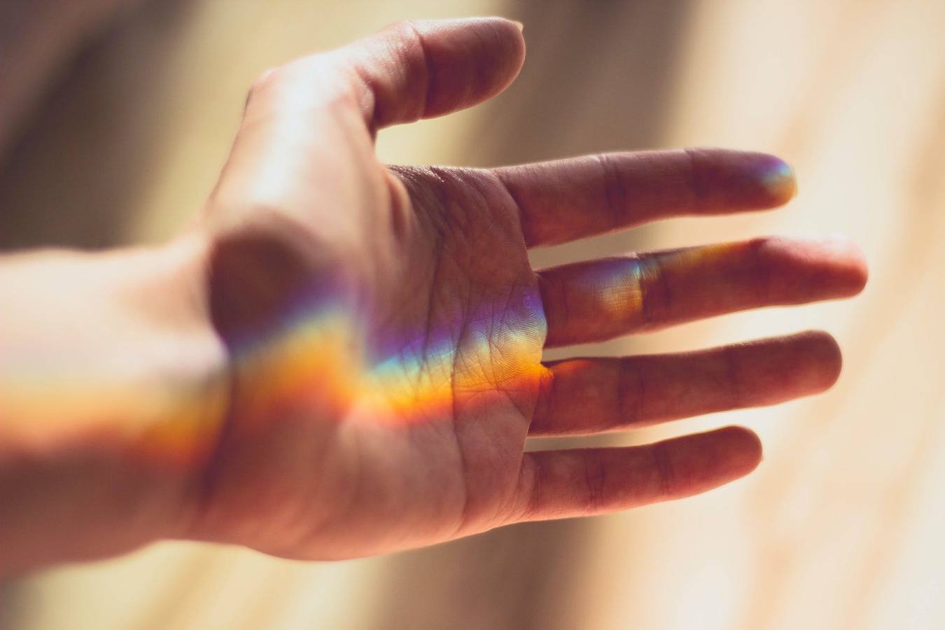 a hand reaching out, it islit up by a line of rainbow spectrum light