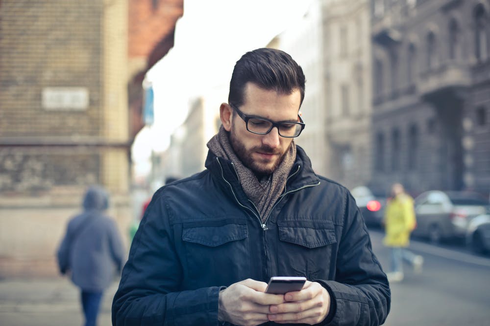 bespectacled man in a coat staring at his phone